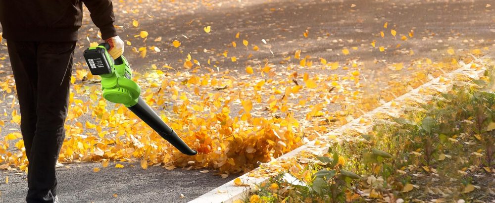 A person cleaning debris with an electric leaf blower.